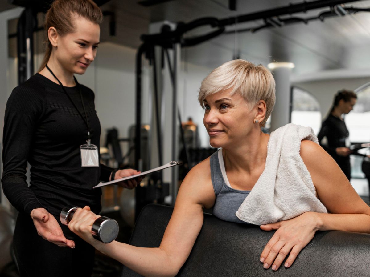 Mulher com mais de 50 anos fazendo musculação com ajuda de personal trainer