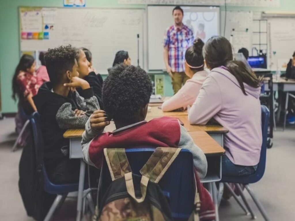Imagem colorida de professor e alunos em sala de aula