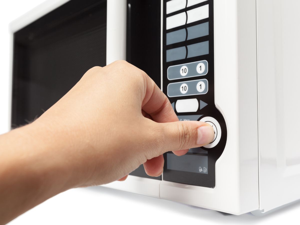 Mão apertando botão de micro-ondas branco