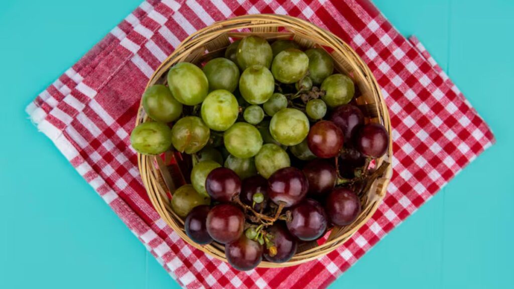 Mesa azul claro com uma toalha xadrez vermelha com uma cesta de uvas verdes e roxas, c
