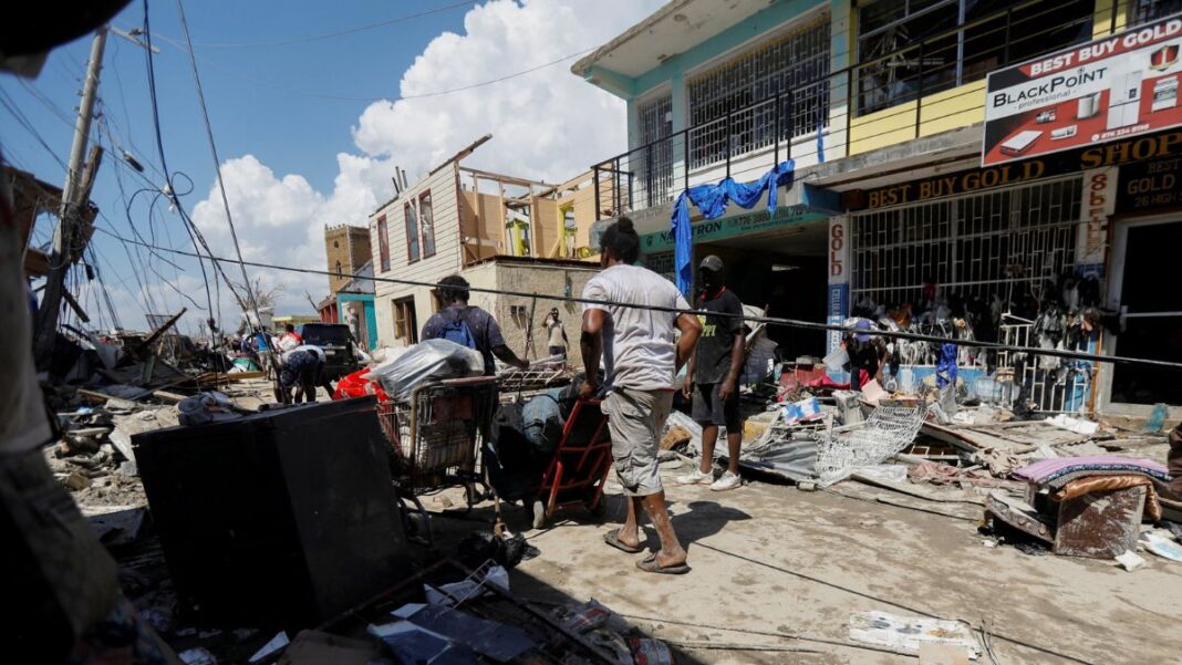 Jamaica Homens empurram carrinhos com pertences em meio a rua destruída pelo furacão