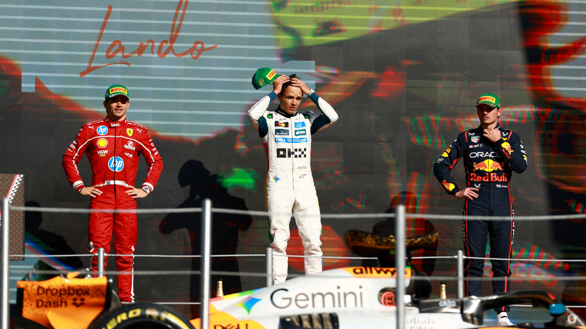 Fórmula 1_GP México 2025_Foto_Reuters Três pilotos de Fórmula 1 estão no pódio após uma corrida. No centro, o vencedor, vestido com macacão branco da equipe McLaren, segura o boné verde da Pirelli sobre a cabeça. À esquerda, um piloto da Ferrari, de macacão vermelho, observa com as mãos na cintura. À direita, um piloto da Red Bull, de macacão azul escuro, mantém a mão no queixo. Em primeiro plano, parte do carro laranja e preto da McLaren aparece, e ao fundo, um telão exibe o nome “Lando”, indicando o vencedor da prova.