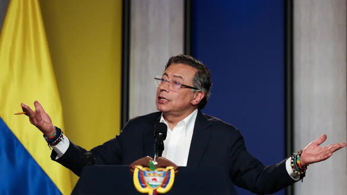Gustavo Petro_Colombia_Foto_Reuters Homem de terno escuro e camisa branca fala em um púlpito com o brasão da Colômbia. Ele está com os braços abertos e expressão séria, olhando para o alto. Usa óculos e várias pulseiras coloridas nos pulsos. Ao fundo, há um painel com as cores da bandeira colombiana — amarelo, azul e vermelho —, sugerindo um pronunciamento oficial.
