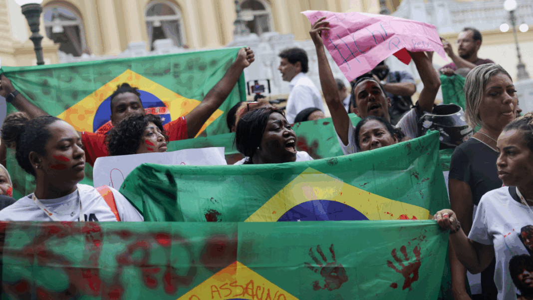 Pessoas erguem bandeiras do Brasil com marcas de mãos pintadas de vermelho em protesto