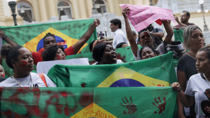 Pessoas erguem bandeiras do Brasil com marcas de mãos pintadas de vermelho em protesto