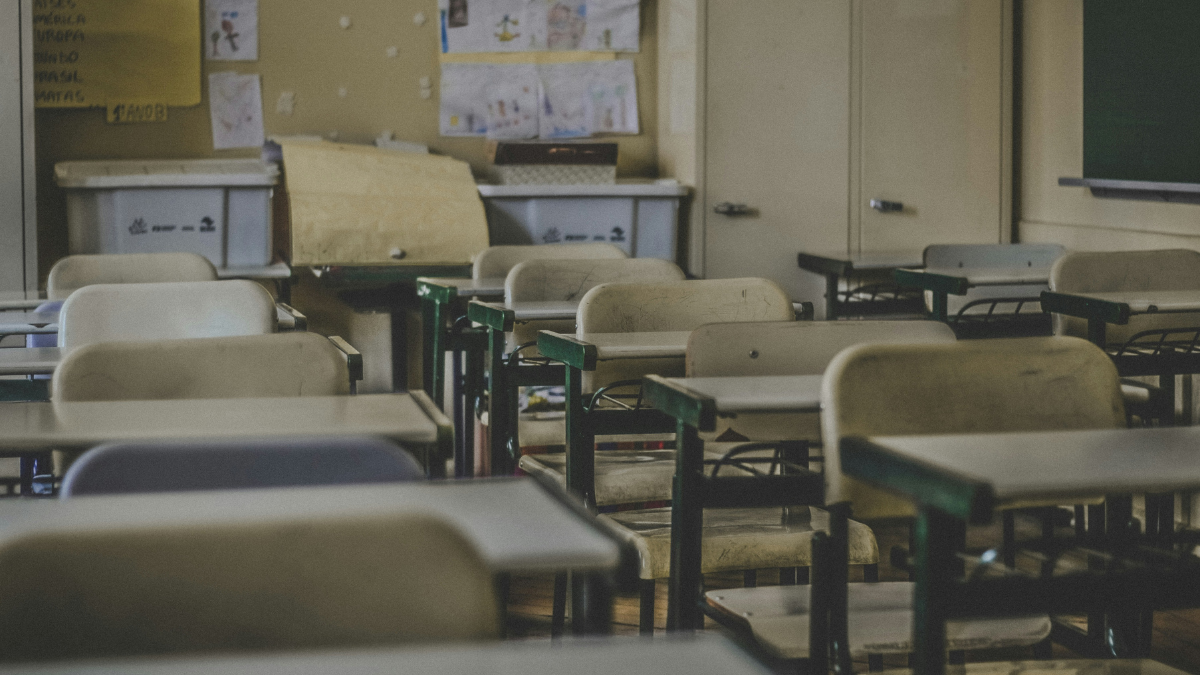 Uma sala de aula com cadeiras e mesas vazinhas, com estantes no fundo.