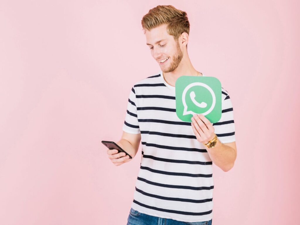 Homem branco segurando um celular em uma mão e na outra o símbolo do WhatsApp.