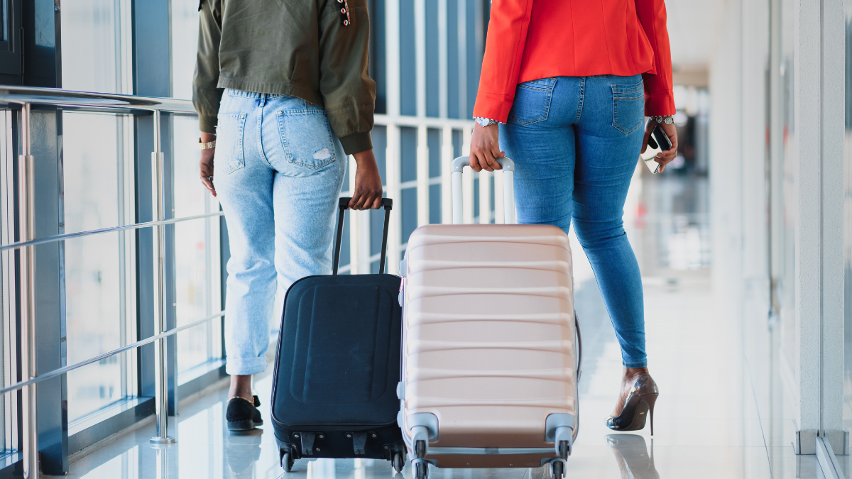 bagagens Duas mulheres caminham pelo aeroporto, cada uma puxando sua mala.