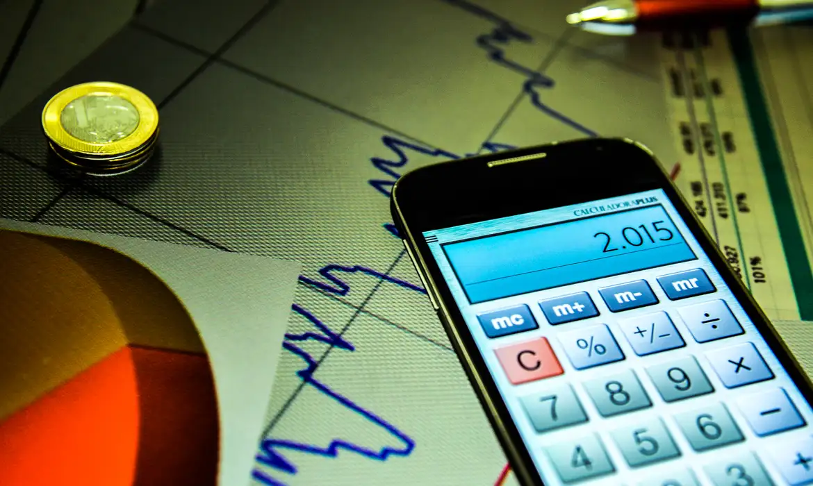 Mercado Financeiro Foto de um celular, com o aplicativo da calculadora aberta, em cima de uma folha com um gráfico genérico