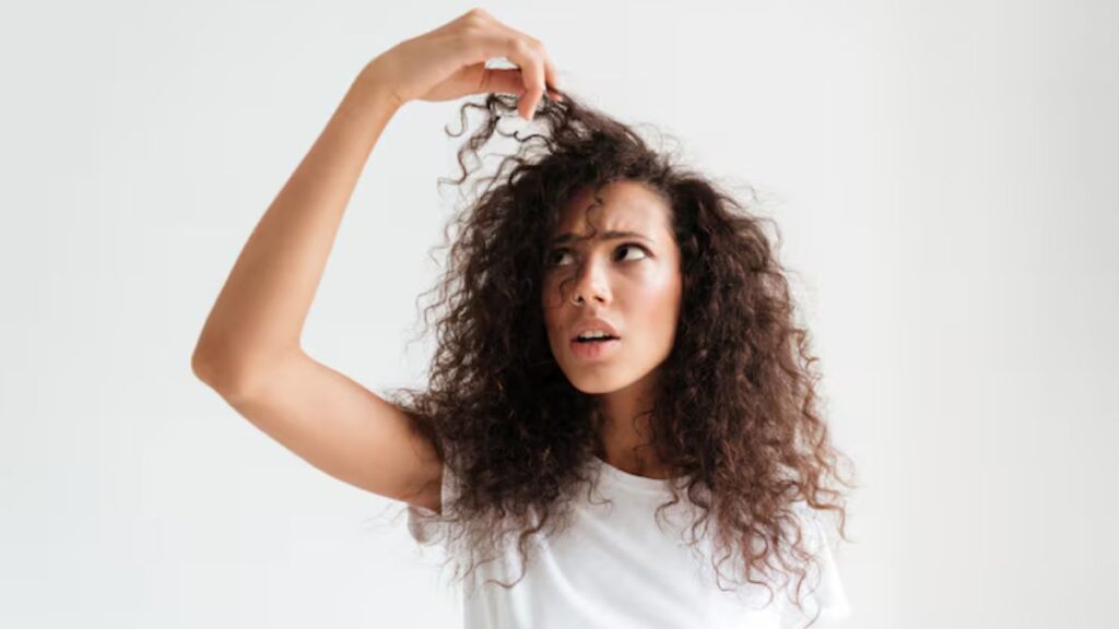 Mulher de cabelo cacheado com rosto de assustada segurando a mecha do cabelo