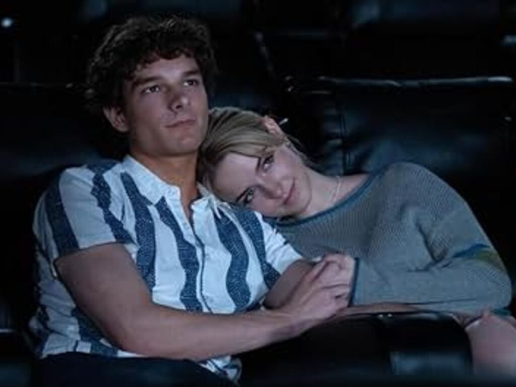 Um casal de jovens estão sentados lado a lado. A garota é branca e loira. O garoto é branco e moreno.