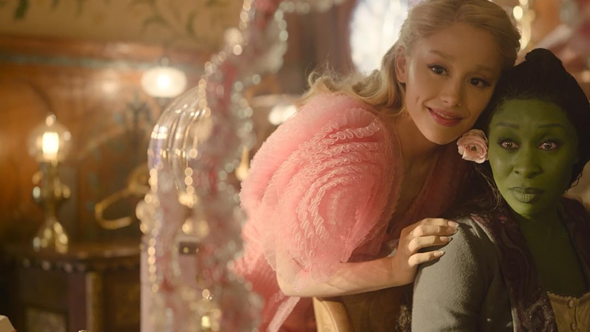 Glinda com a mão no ombro de Elphaba, enquanto ambas se olham no espelho
