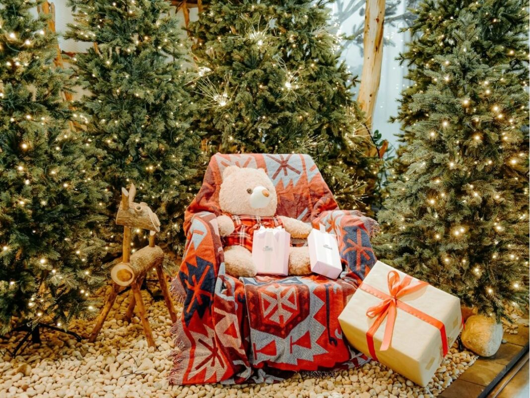 Poltrona com urso de pelúcia e várias árvores natalinas em volta.