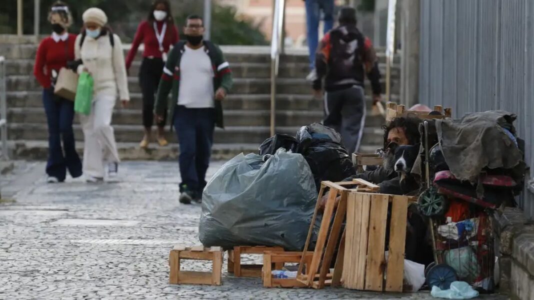Mulher em situação de rua limpa a entrada de sua barraca