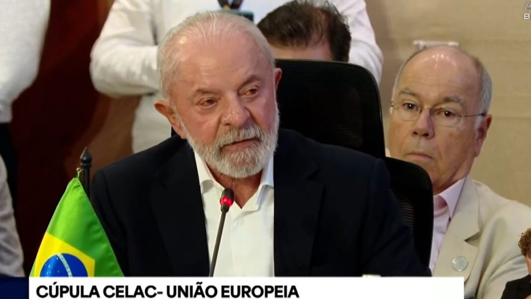 Lula, sentado de terno azul marinho e camisa branca, discursando