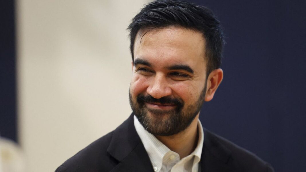 Zohran Mamdani de blazer escuro e camisa branca, sorrindo