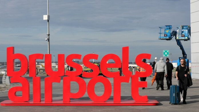Pessoas caminham ao lado de uma placa no Aeroporto de Bruxelas.