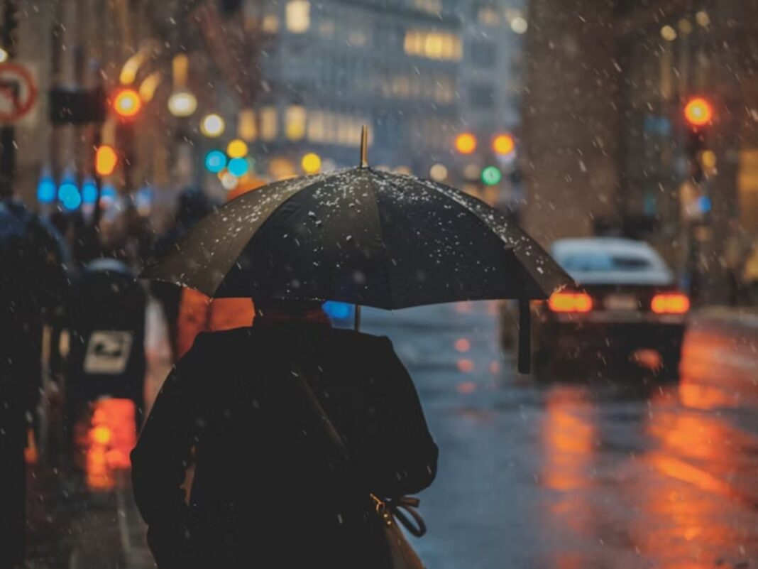 A imagem mostra uma pessoa de costas usando um guarda-chuva na rua enquanto chove muito