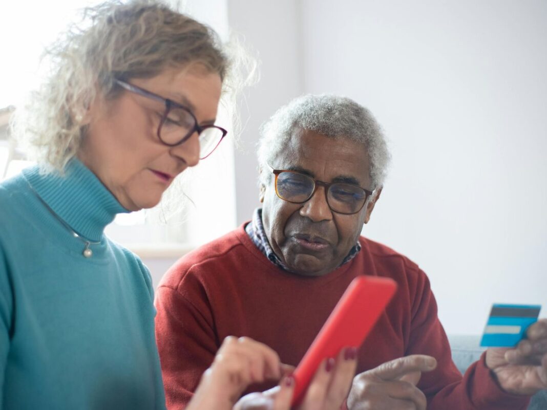 Em imagem ilustrativa, dois idosos consumindo produtos via celular