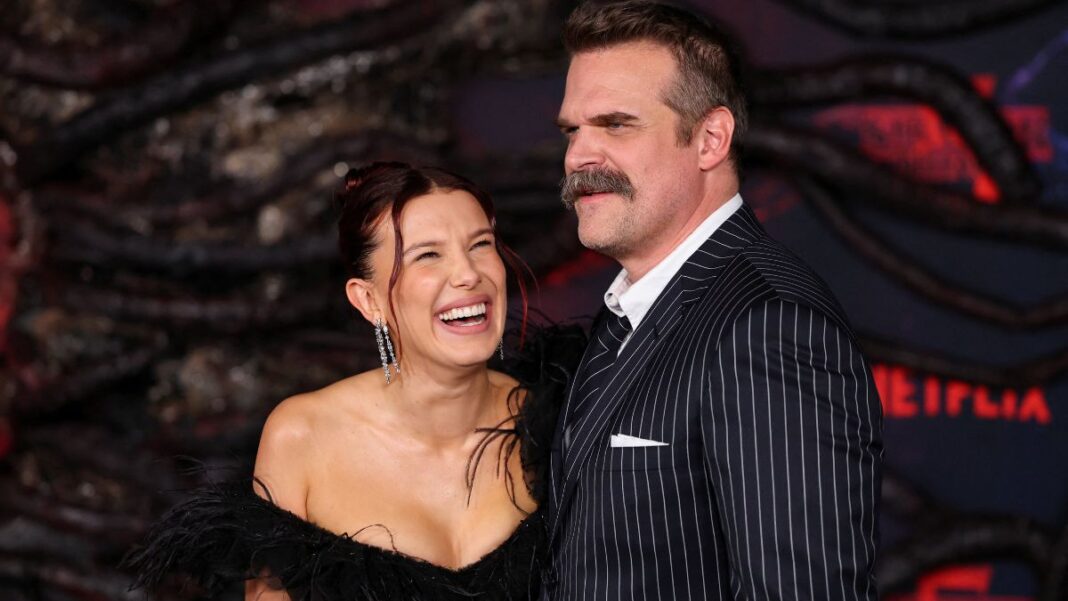 Imagem mostra os atores Millie Bob Brown e David Harbour abraçados e rindo durante o Stranger Things Day.