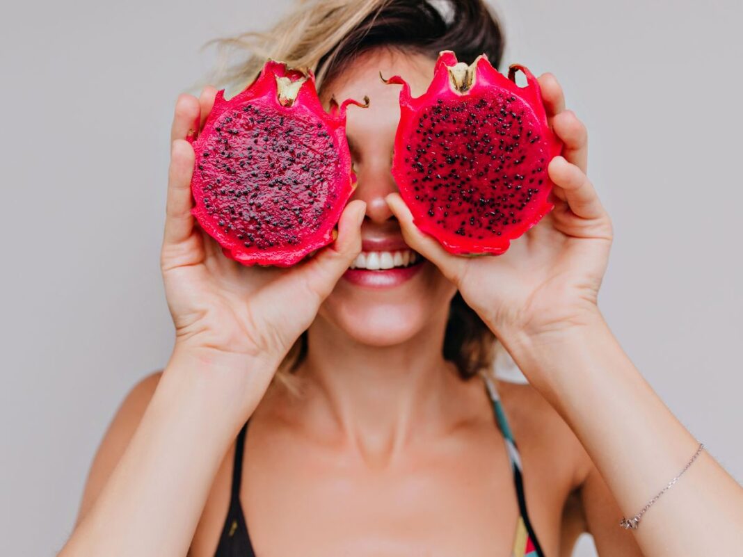 Em imagem ilustrativa, mulher segura uma Pitaya partida ao meio ,acima dos seus olhos.