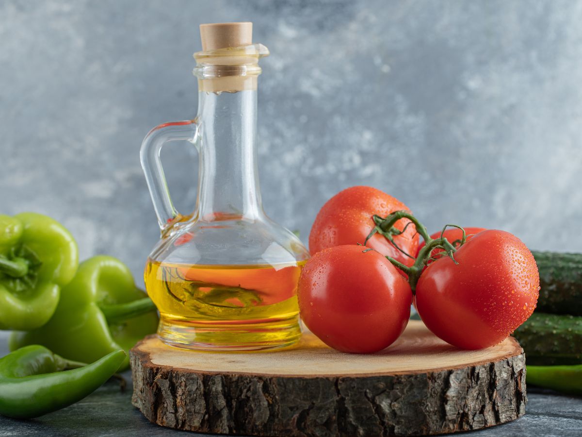 Há um frasco de vidro e dentro dele azeite. Ao lado tem dois tomates e um pimentão verde. 